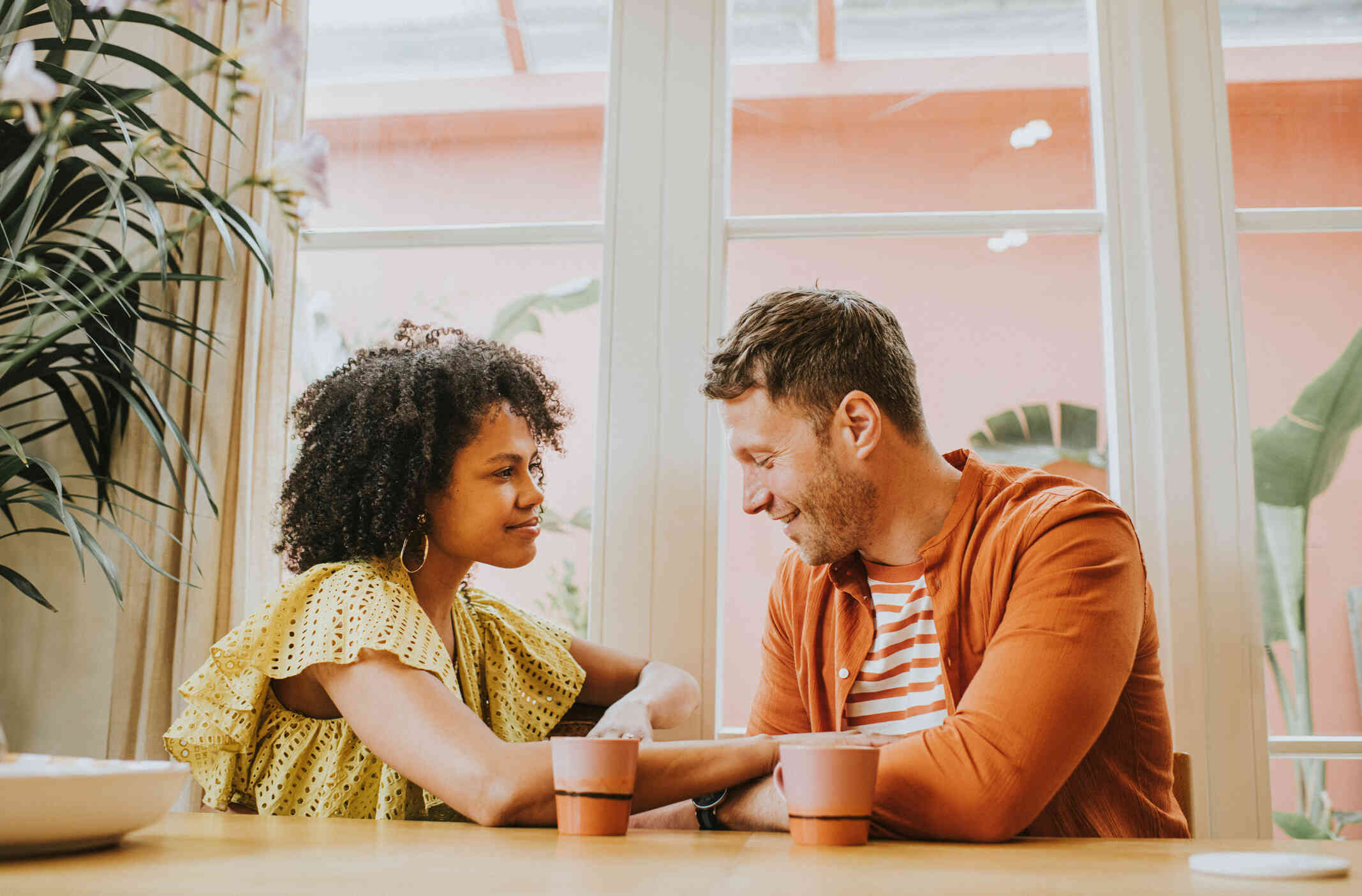 A male and female couple sit next to each other at the table and hold hands while smiling at one another.